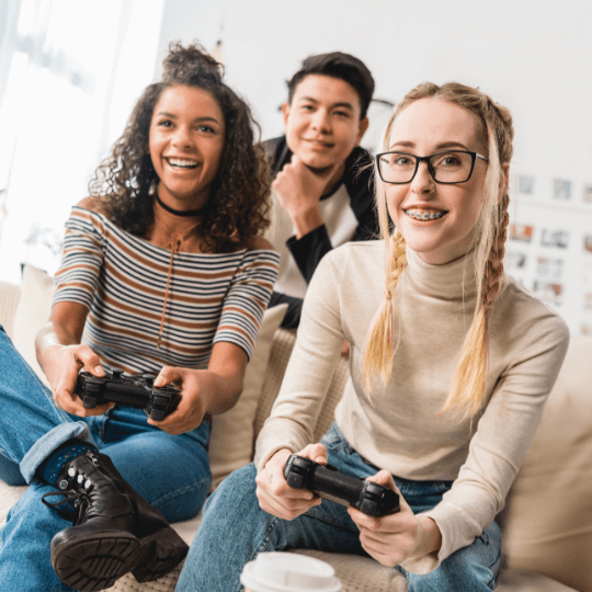 Two adolescents playing a video game while a third watches.